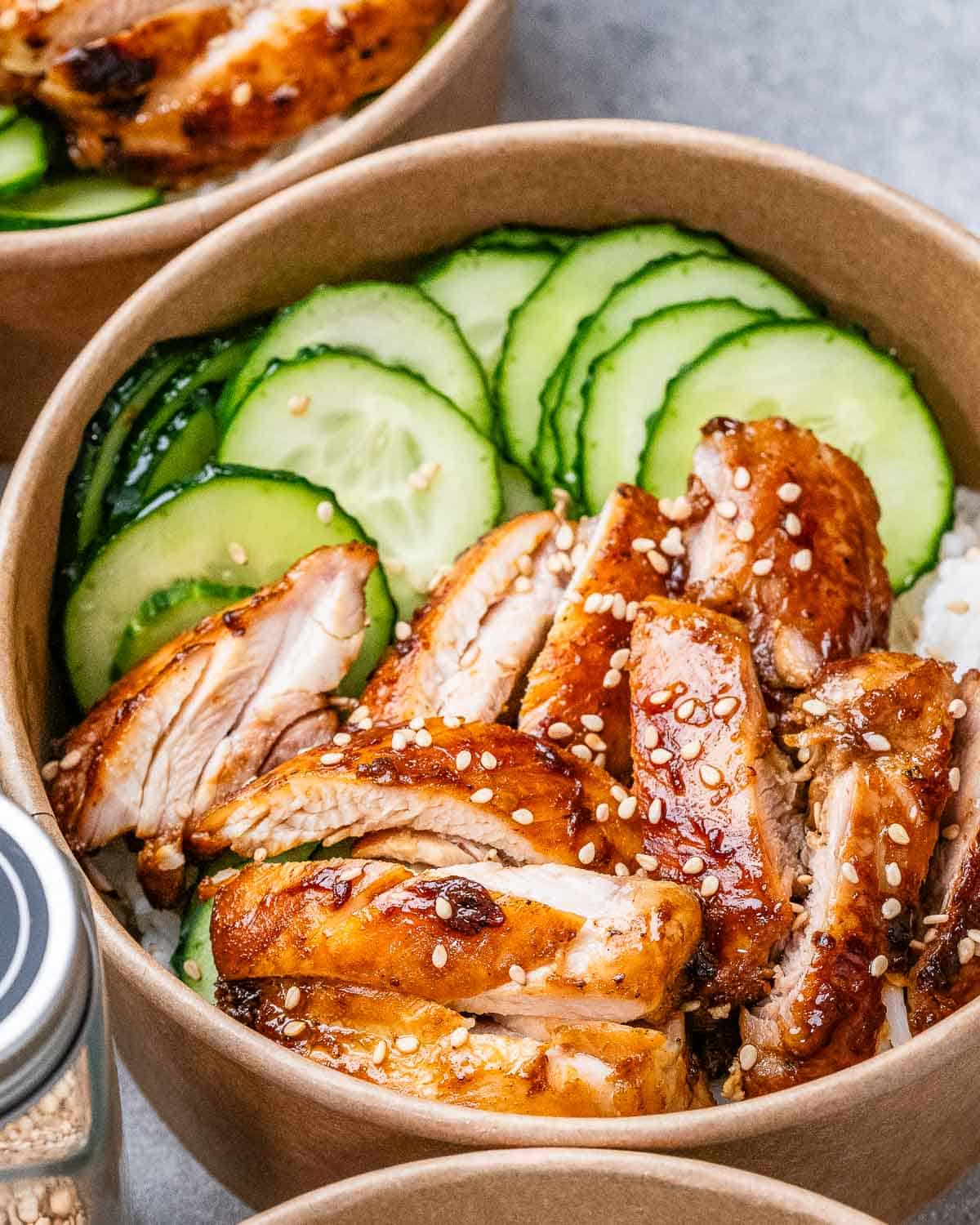 A round bowl with sliced chicken and cucumber is served with white rice.