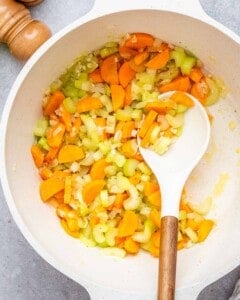 sauteeing vegetables in white round pot with spoon