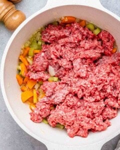 round white pot with raw ground beef, carrots, onions, and celery