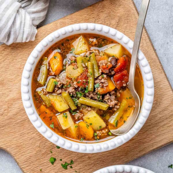 a white round bowl with soup with veggies and a spoon in the bowl.