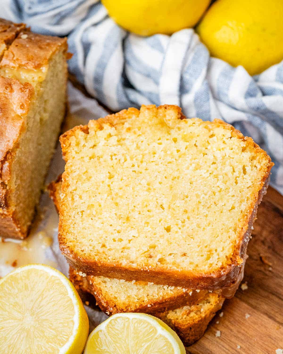 3 sliced lemon cake stacked over each other on a brown cutting board with lemon slices next to it.