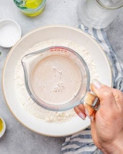 a container of activated yeast liquid mixture over a bowl of flour