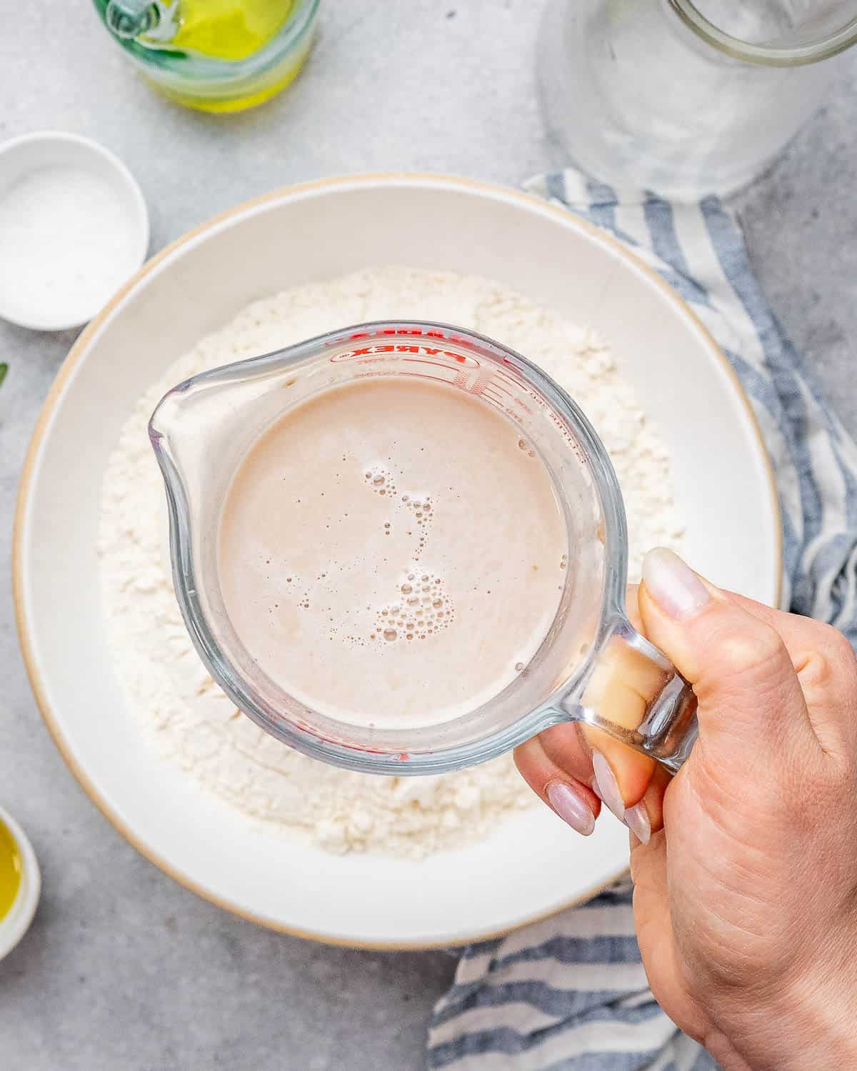 a container of activated yeast liquid mixture over a bowl of flour