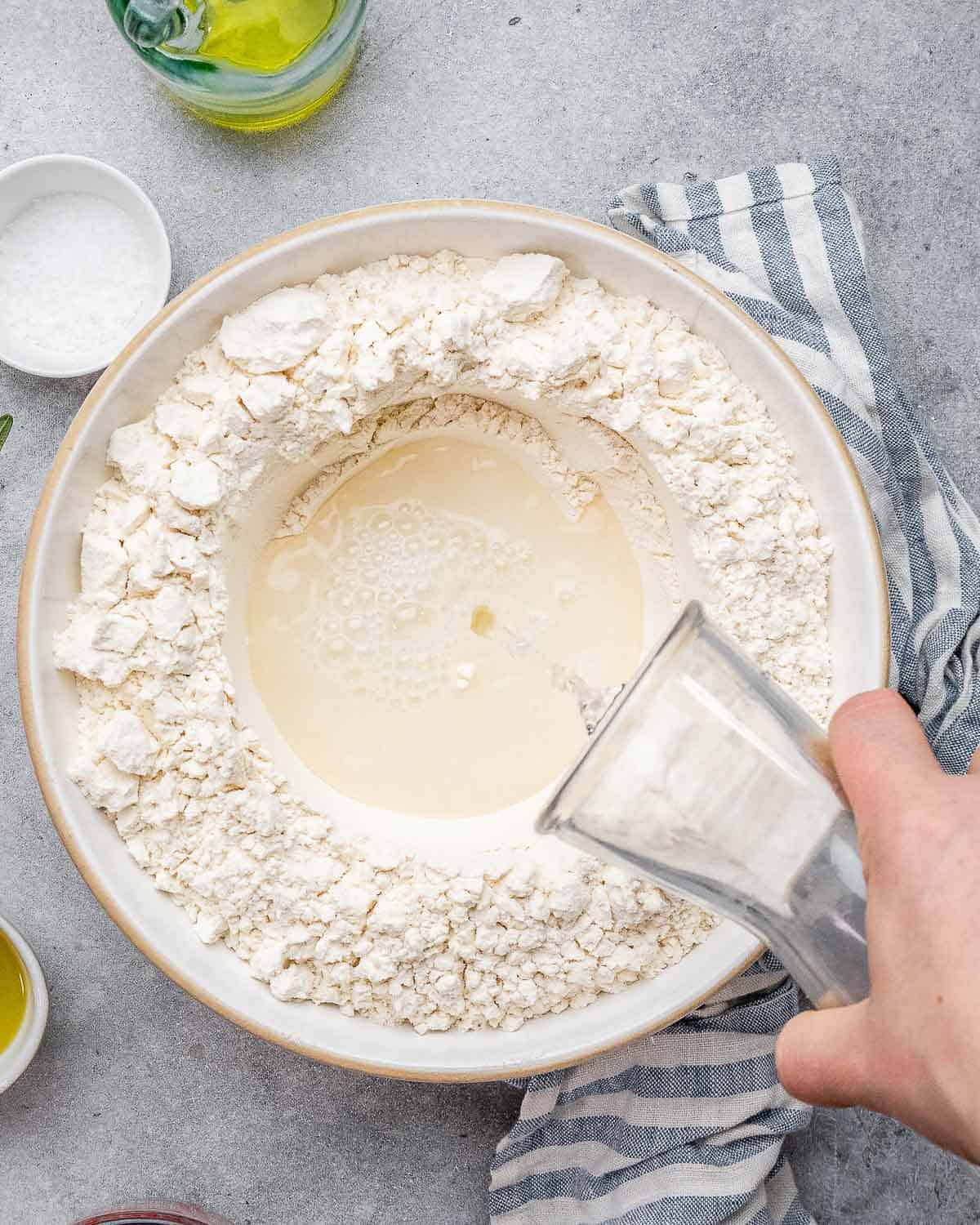 pouring activated yeast, sugar, salt, and water over a bowl of flour