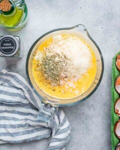 A measuring cup filled with eggs, cheese, and spices.