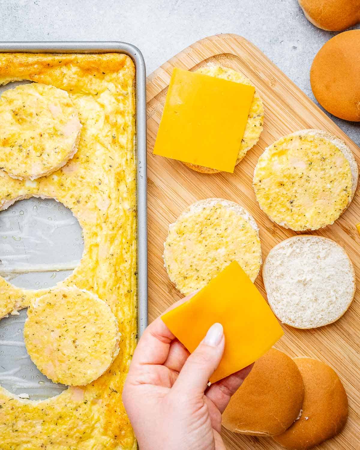 A hand assembling the ingredients to make a sandwich with cheese, eggs, and bread,