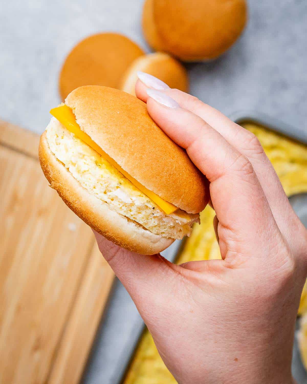 A hand holding a breakfast sandwich over a cutting board.