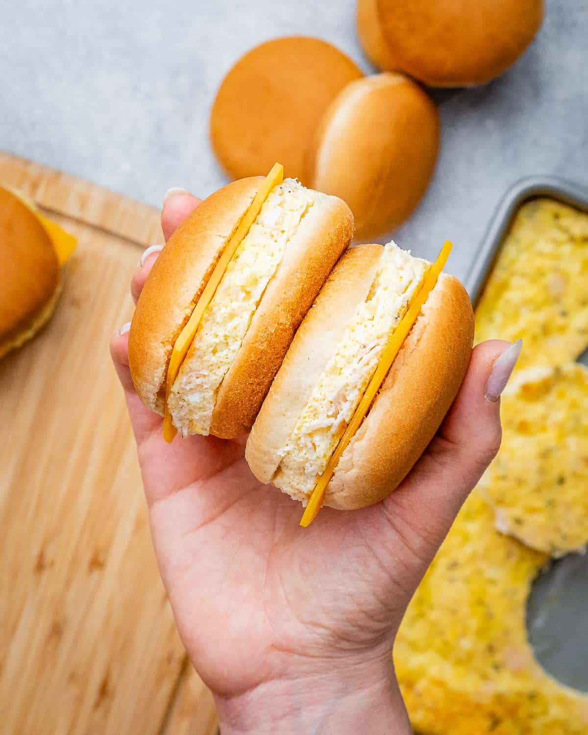 A hand holding two sandwiches back to back over a cutting board.