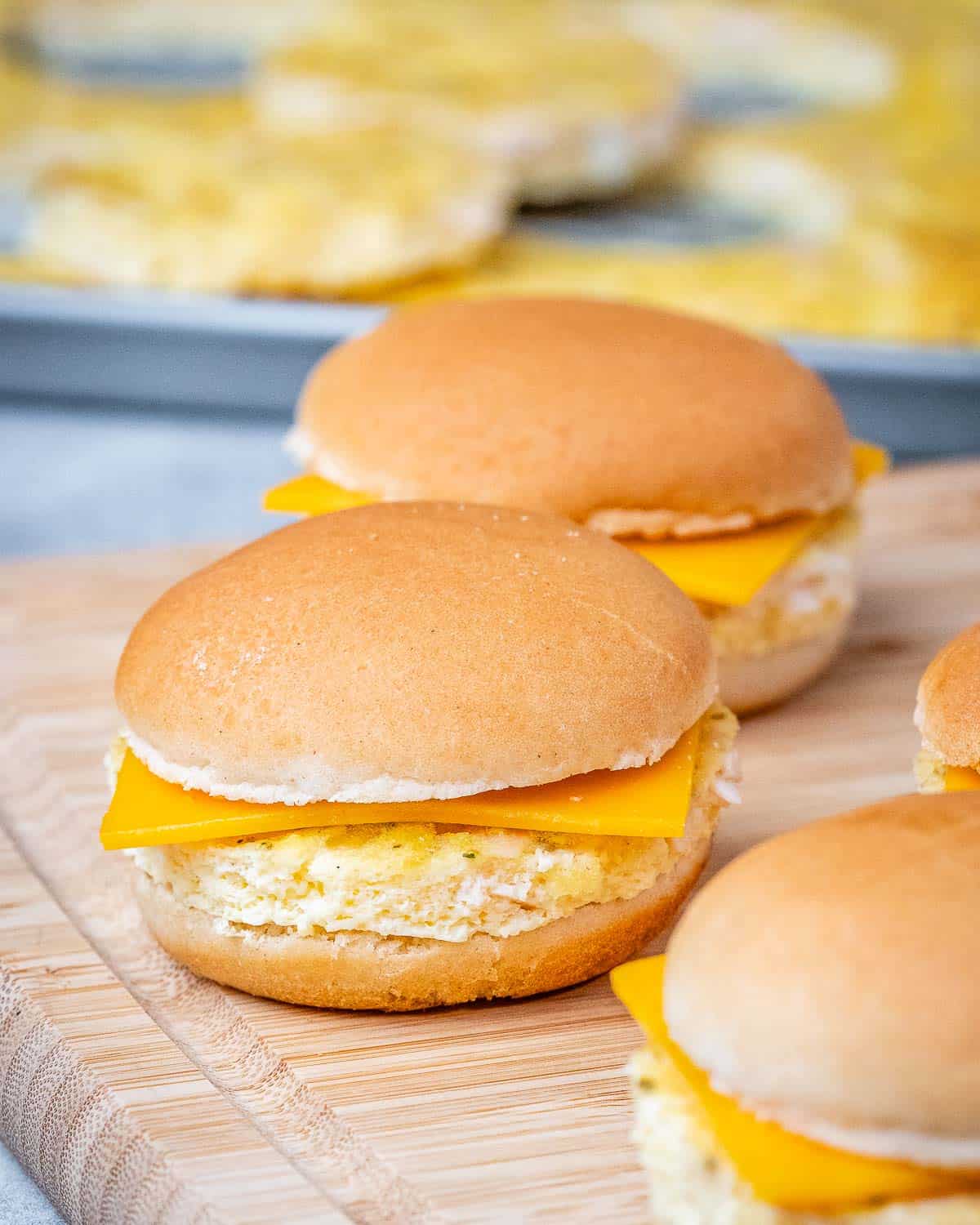 Three sandwiches with cheese on a cutting board.