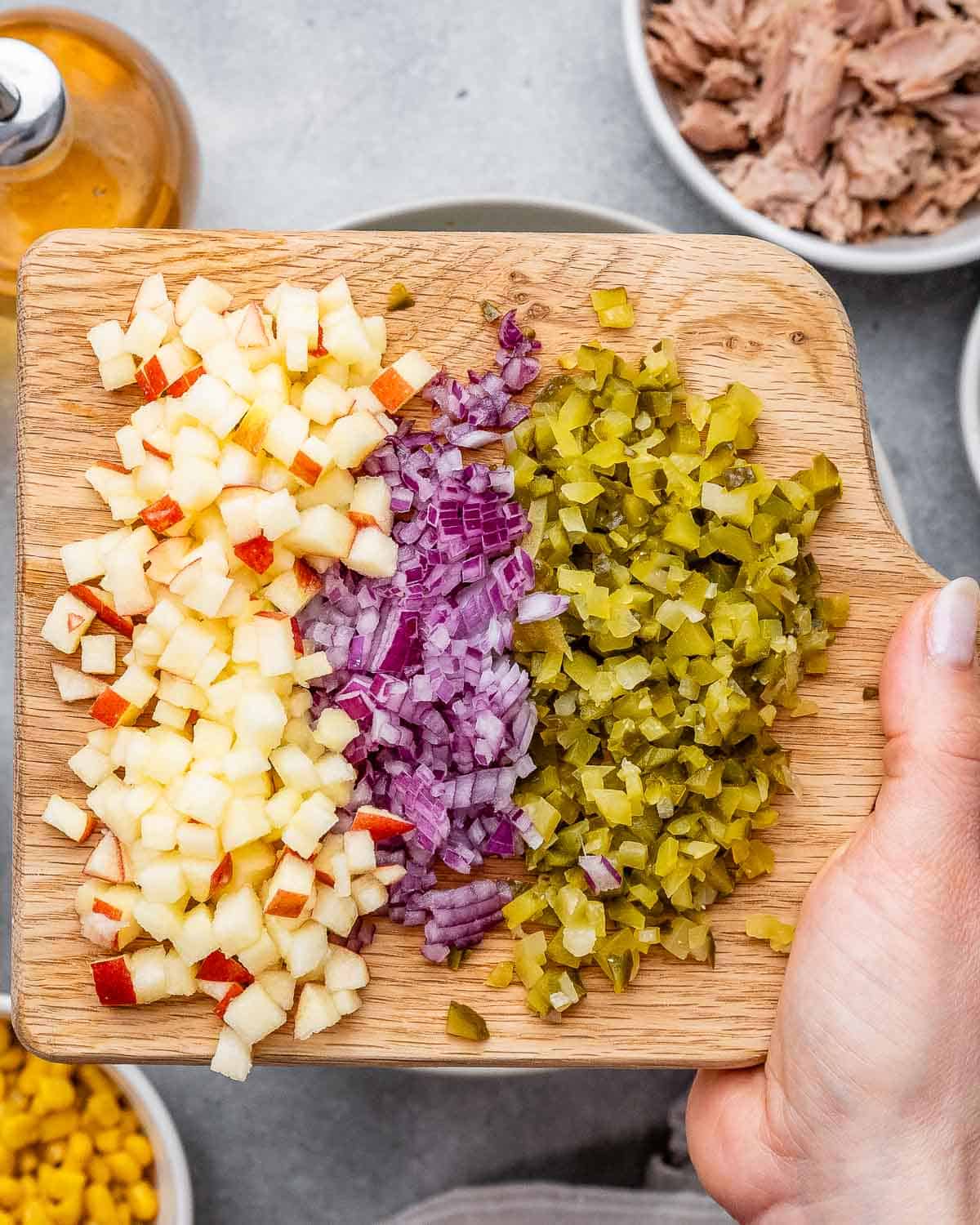 Cutting board with freshly chopped apple, red onion, pickles, and crushed jalapeño chips.