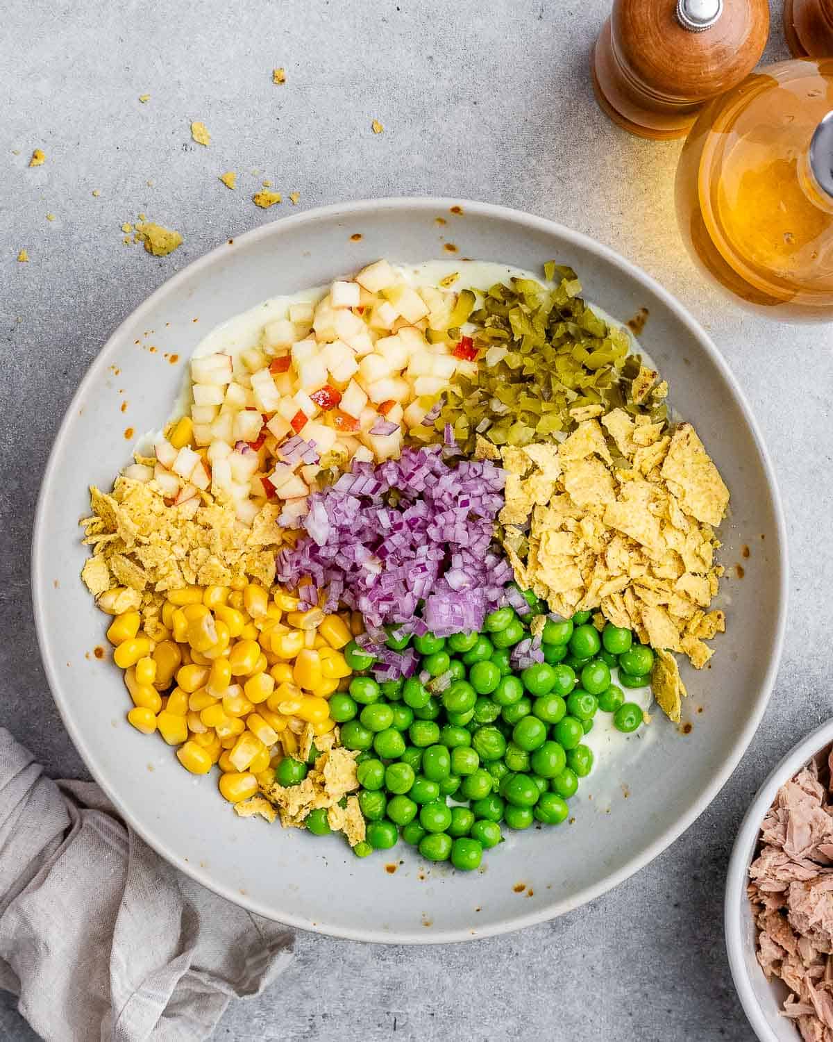 Neatly arranged chopped ingredients including peas, corn, red onion, apple, and pickles before mixing.