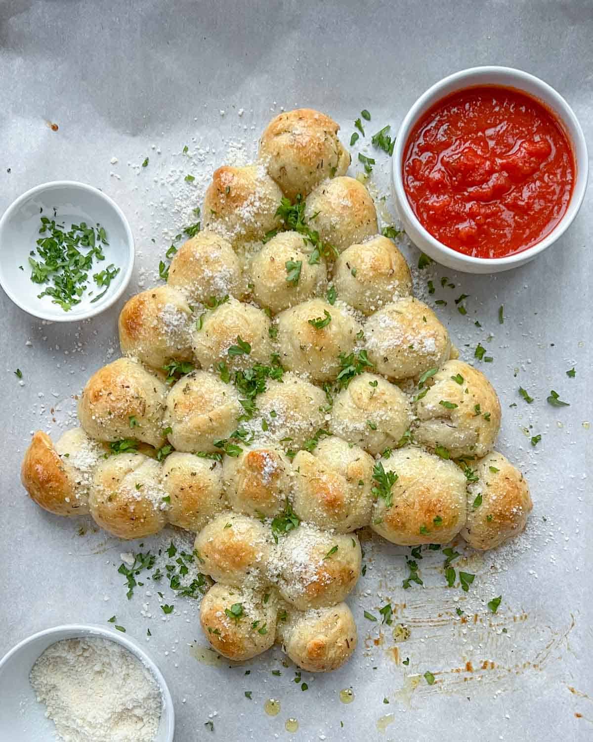 Christmas tree-looking baked pull-apart cheese bread with a bowl of marinara sauce and a bowl of grated mozzarella.