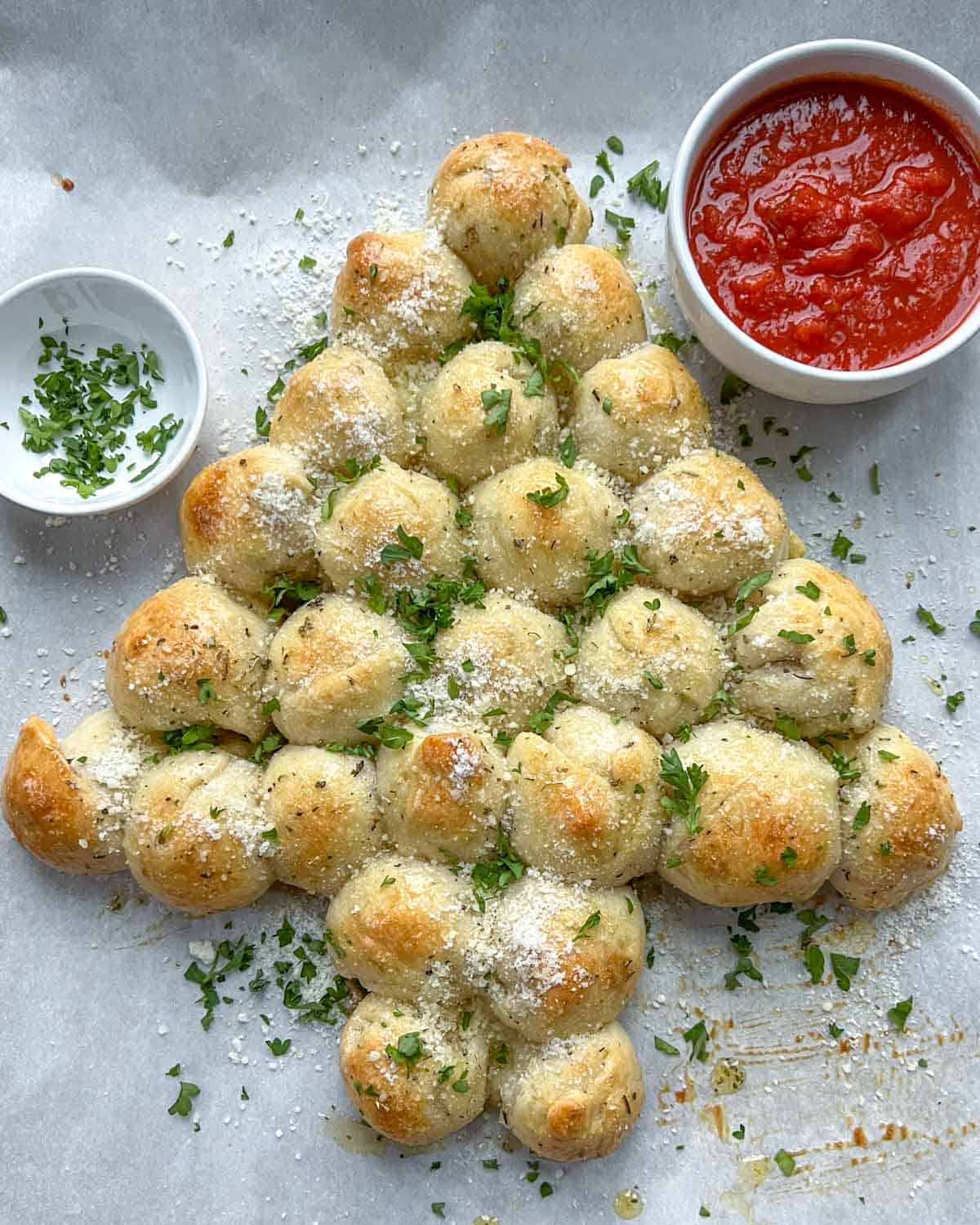 Sheet pan with baked cheese ball pull-apart bread that is made to look like a Christmas tree with a marinara sauce bowl next to it.