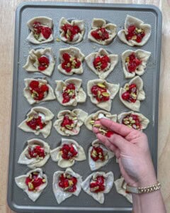 pistachio being topped over the cranberry brie bites in muffin pan.