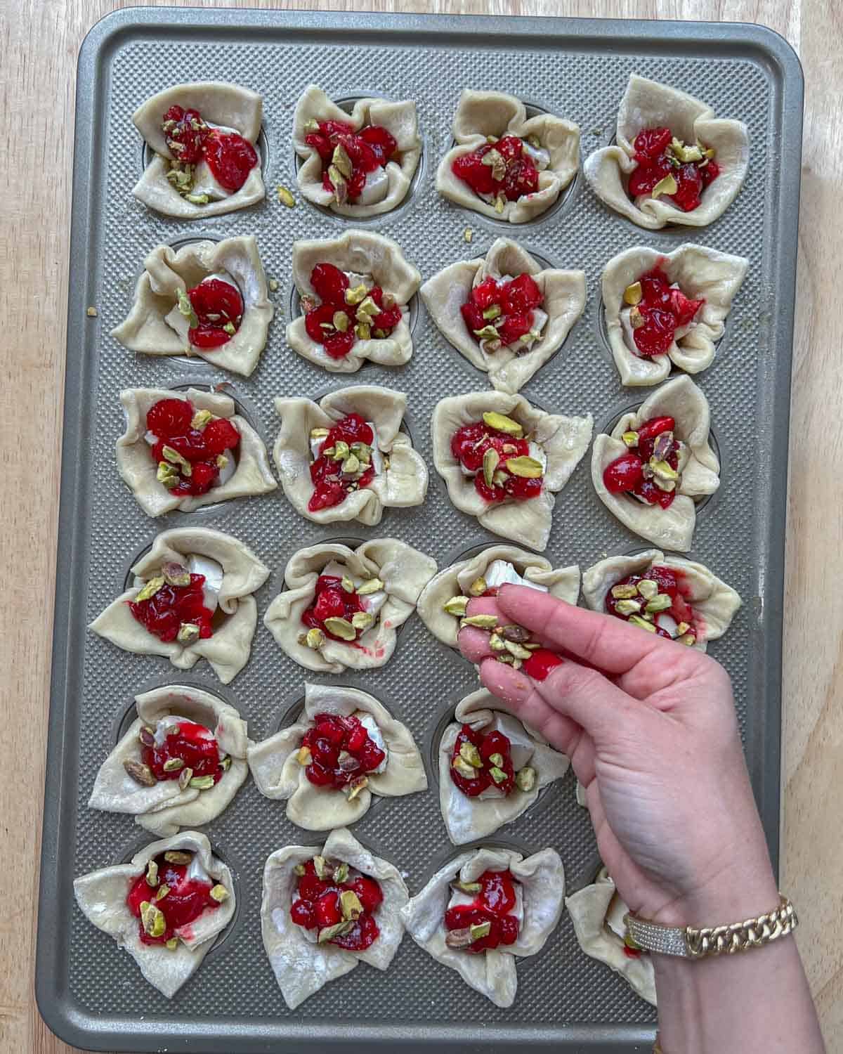 pistachio being topped over the cranberry brie bites in muffin pan.