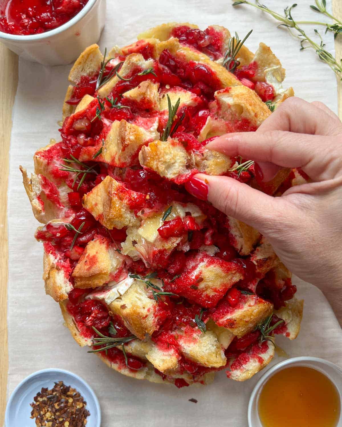 hand grabbing a piece of bread with cranberry sauce and melted brie cheese.