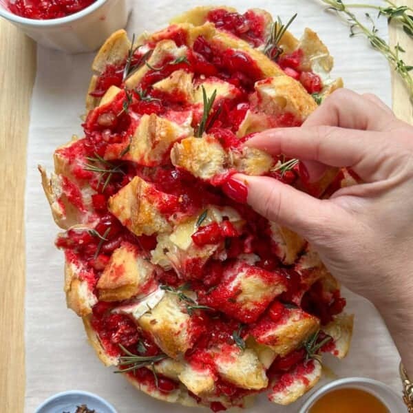 Pull apart bread with cranberry and brie and a hand grabbing a bite.