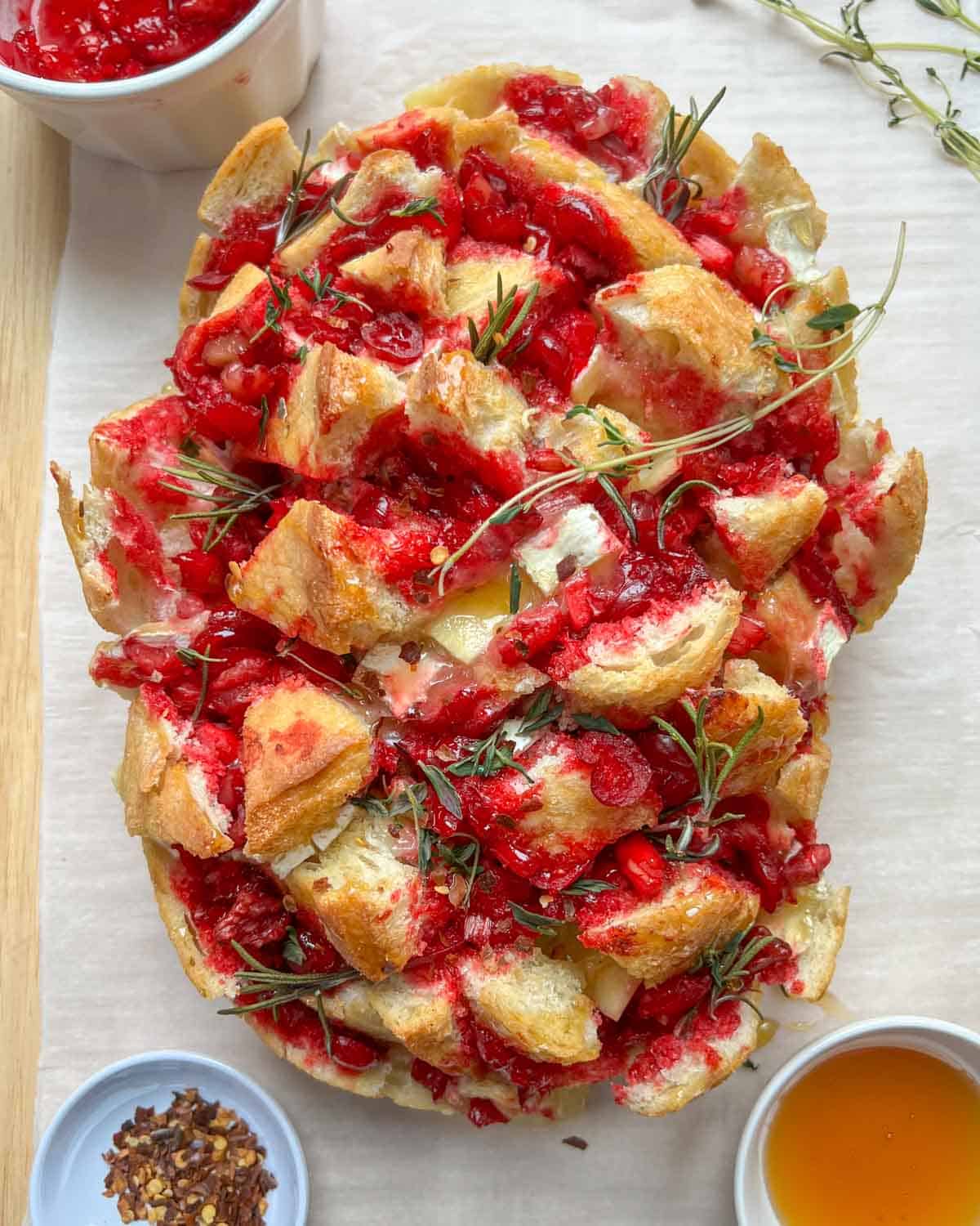 cranberry bread on a sheet pan with a small bowl of honey, and a bowl of cranberry sauce.