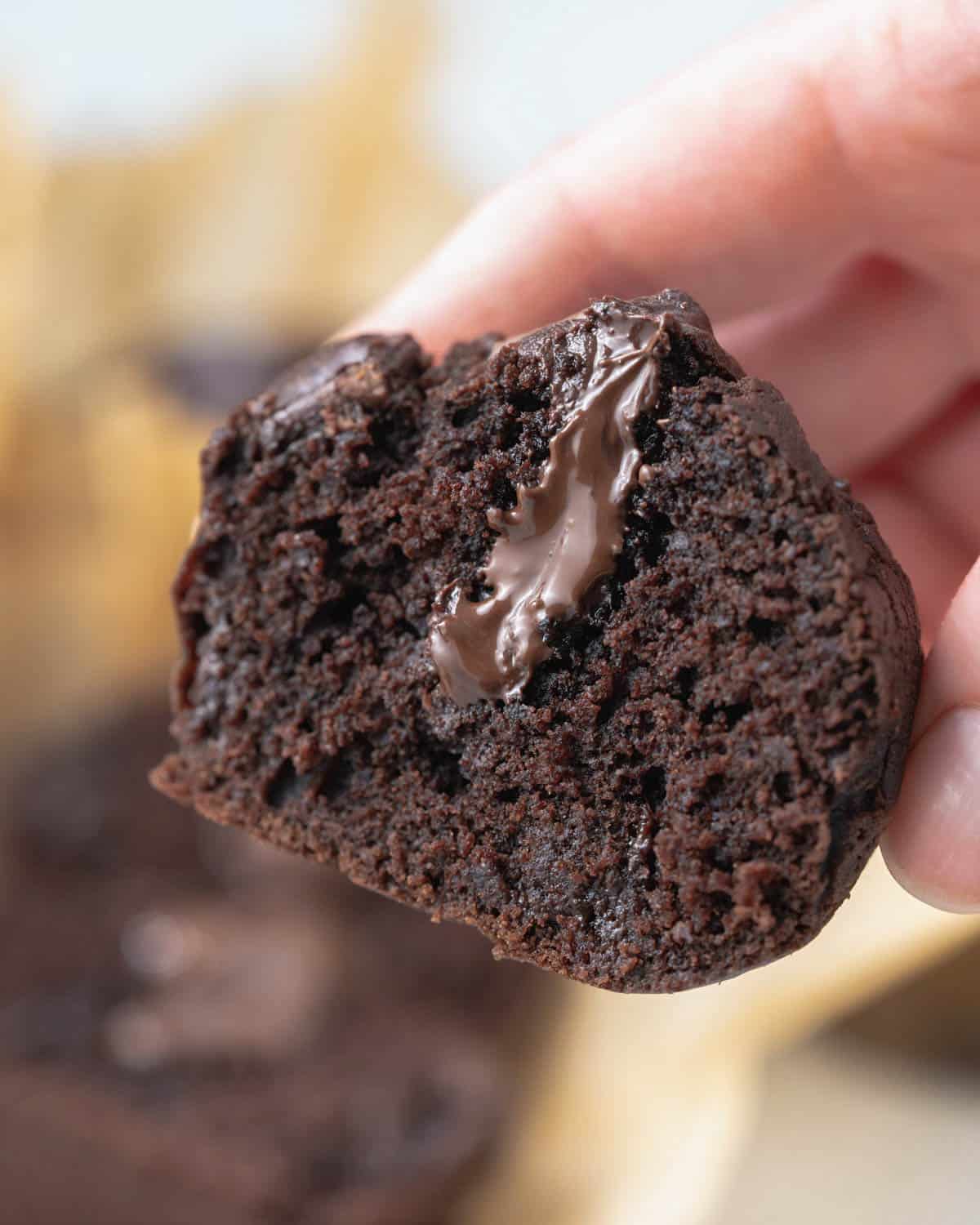 hand holding a chocolate muffin cut in half and chocolate ganache in the middle.