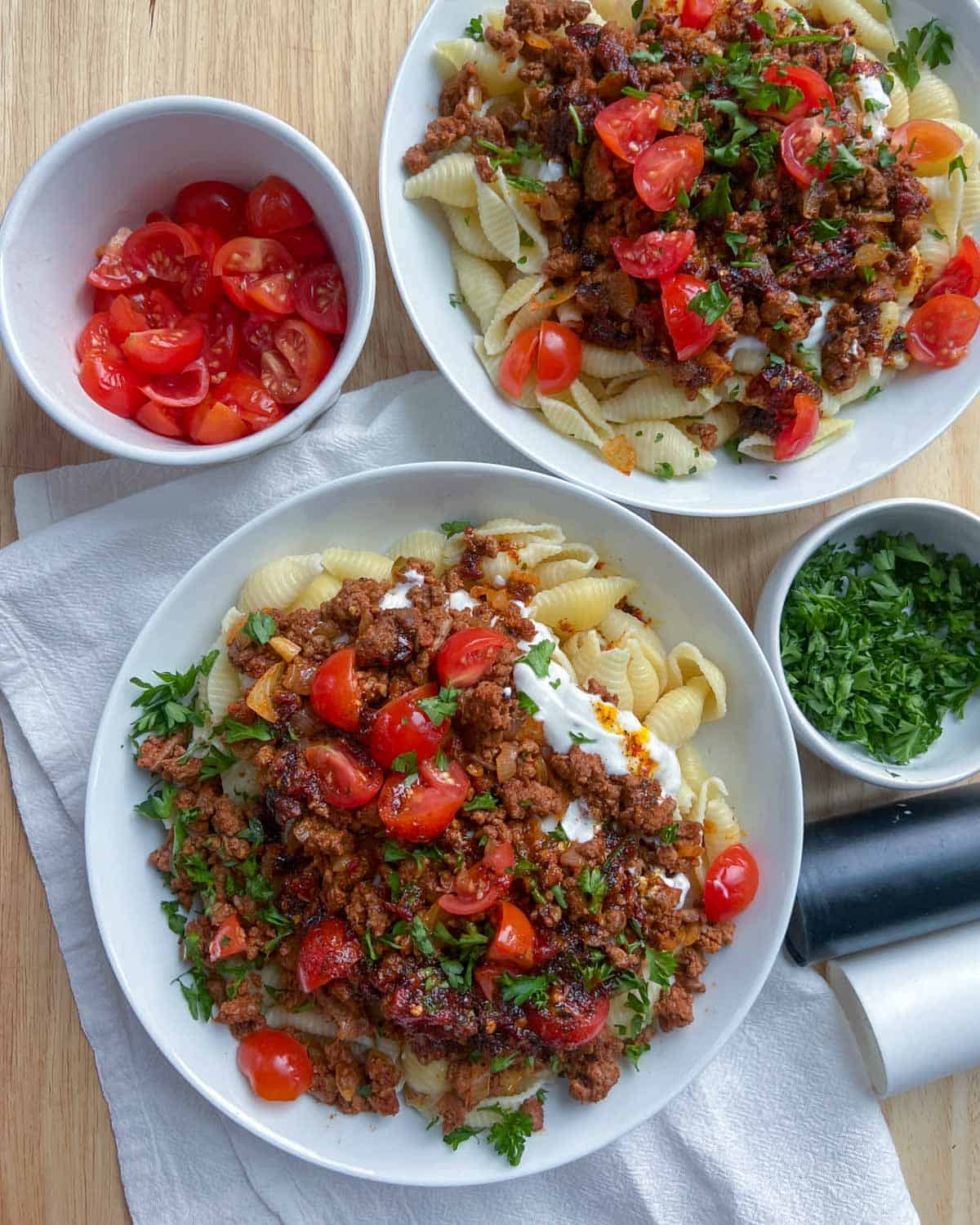 Two plates full of Turkish pasta with two small bowls that have tomatoes and parsley in them.