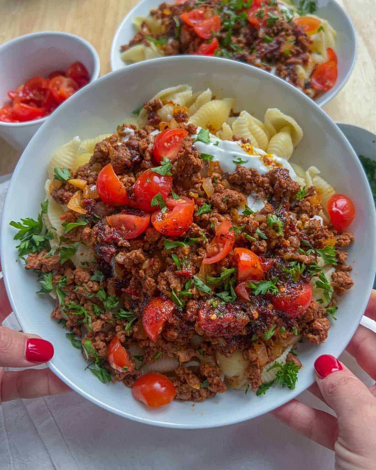 hand holding a plate of Turkish pasta topped with chopped tomatoes and parsley.