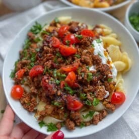 Pasta topped with seasoned beef and garnished with chopped tomatoes and chopped parsley in a dish.