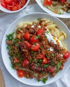 assembled Turkish pasta in a white dish topped with chopped tomatoes and parsley.