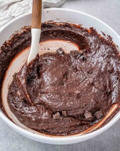 chocolate chunks are added to the brownie batter in a white bowl.