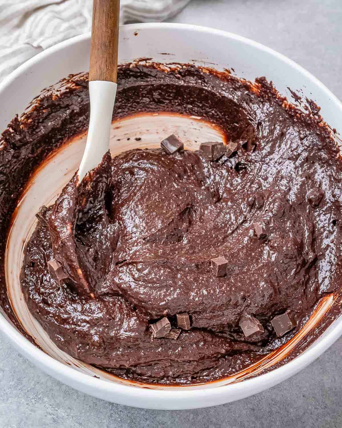 chocolate chunks are added to the brownie batter in a white bowl.