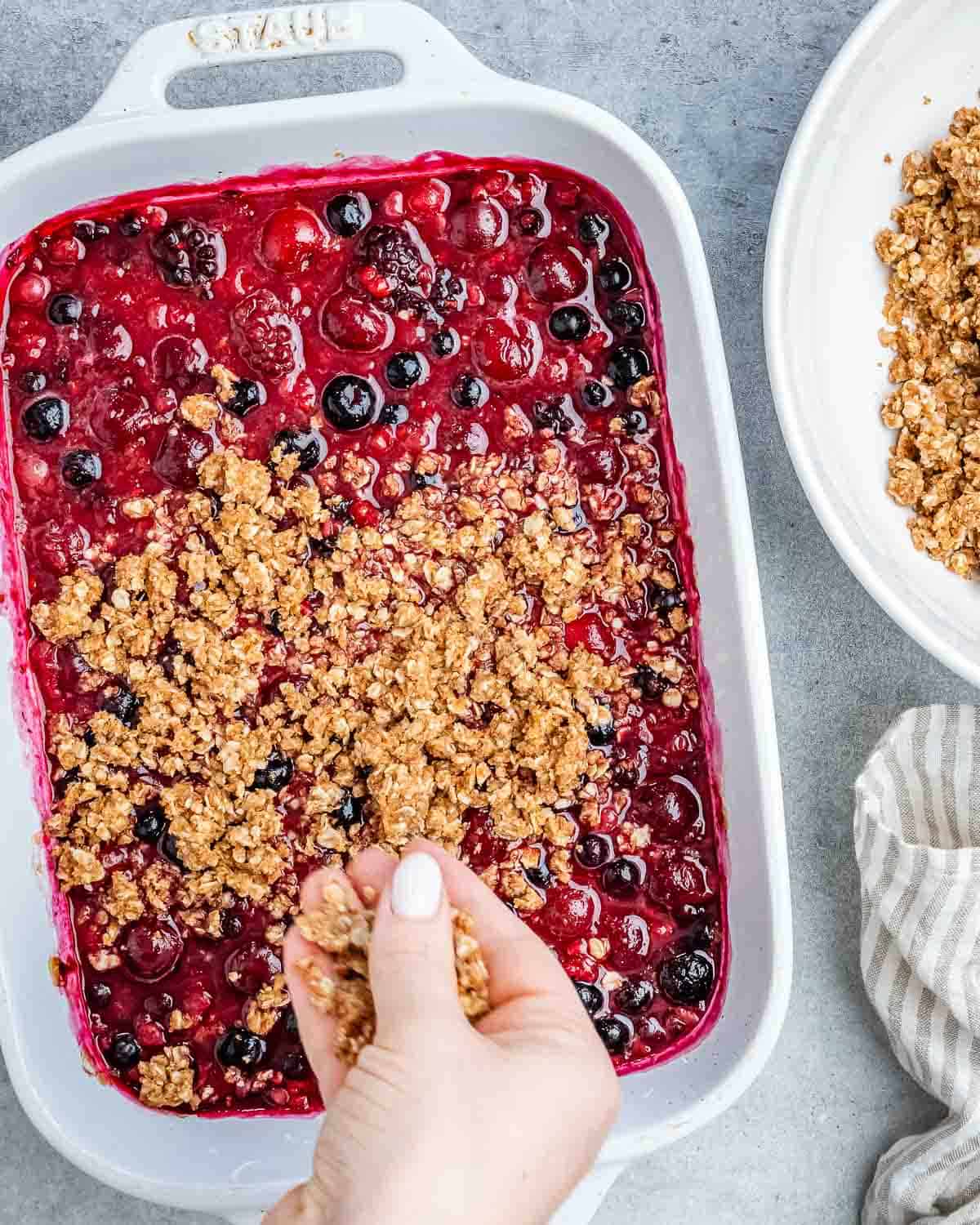 Hand adding the oat mixture over the berry mixture.