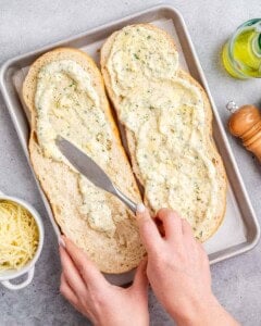 Hand using a spatula and spreading the garlic sauce on sliced bread.