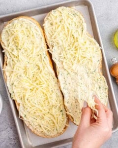 hand adding shredded cheese over sliced bread.