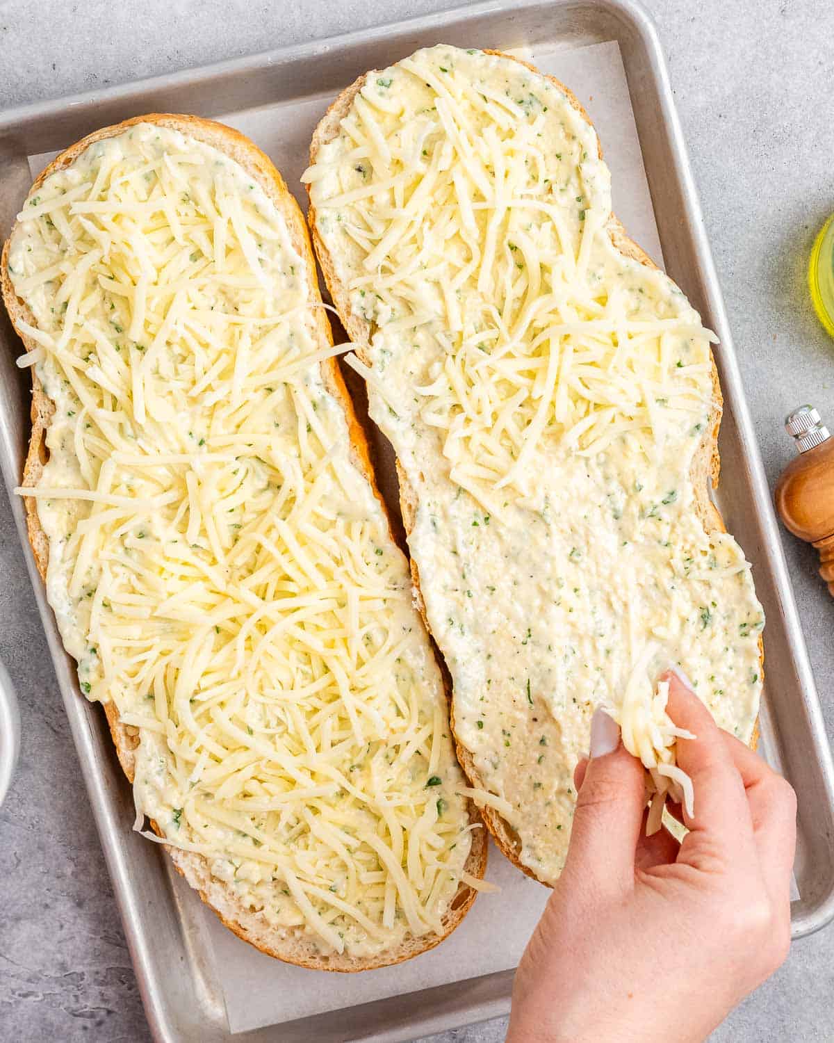 hand adding shredded cheese over sliced bread.