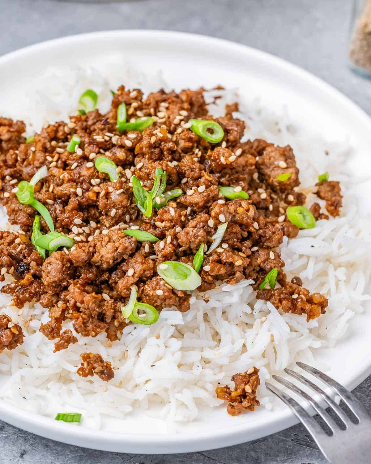 A white plate with rice and ground beef with a fork on the side.