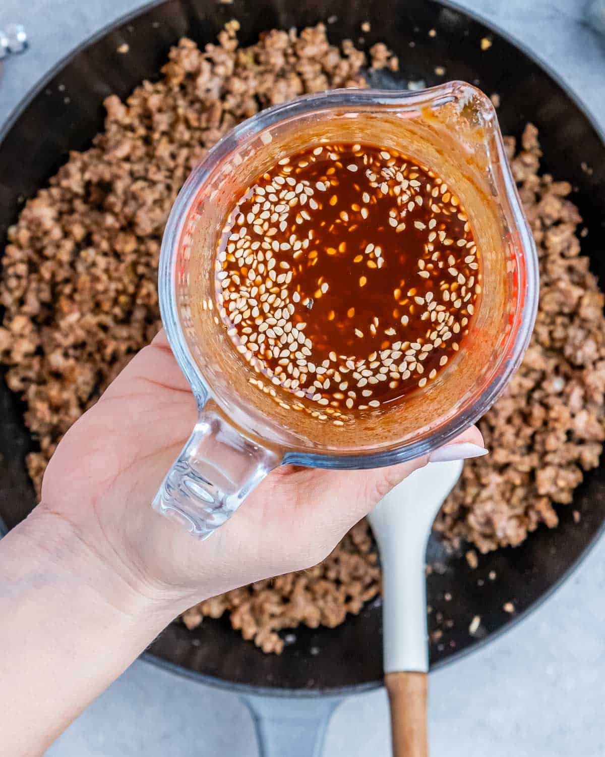 A hand holding liquid over a skillet of ground beef.