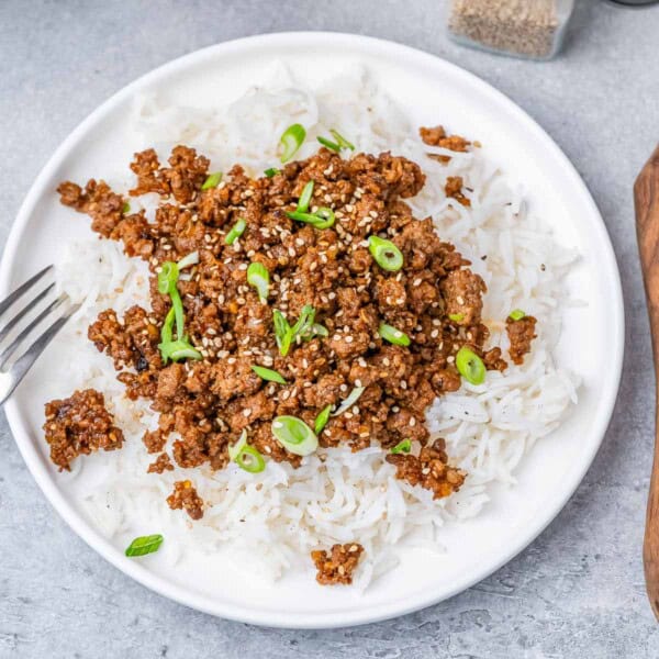 A round plate with white rice topped with sauteed ground beef and sliced green onions.