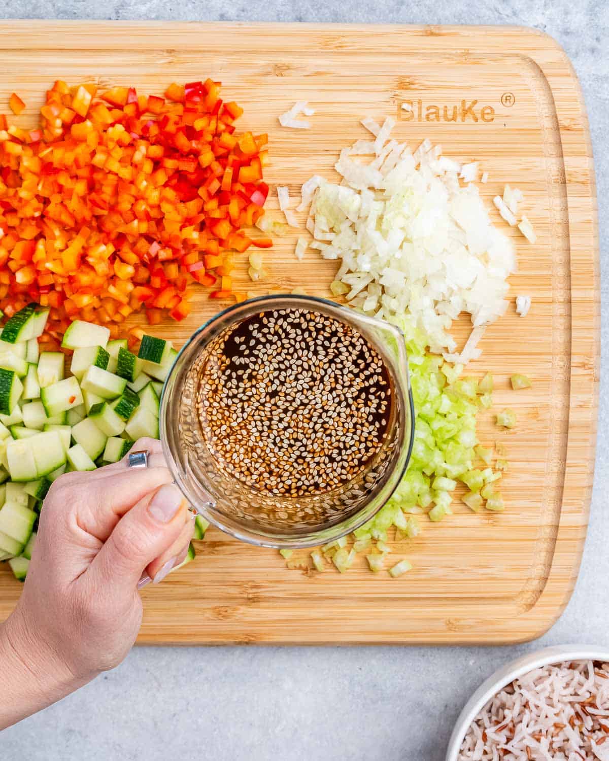 A hand holding a cup of liquid over a cutting board of chopped vegetables.