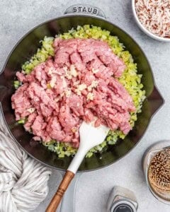 Stirring raw ground turkey with a white spatula in a skillet.
