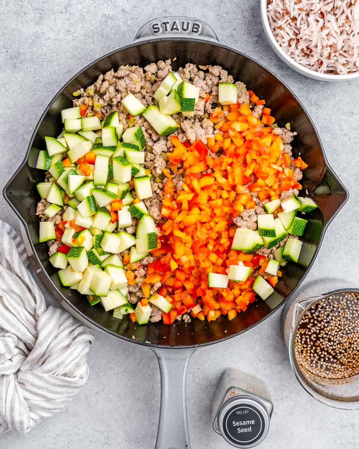 Brightly colored vegetables on top of ground turkey in a skillet.