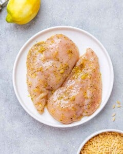 Two raw chicken breasts on a white plate.