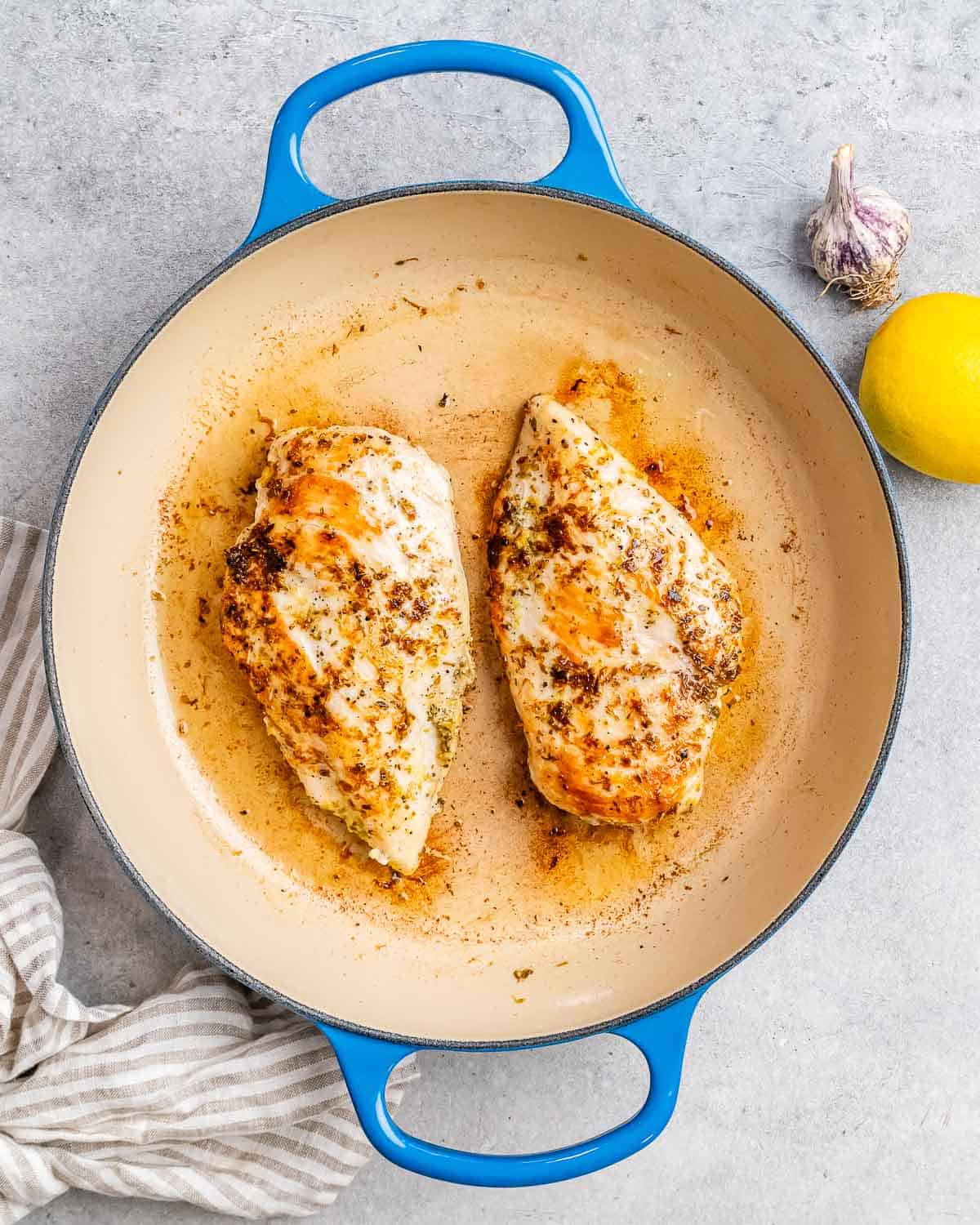 Two chicken breasts searing in a blue skillet.