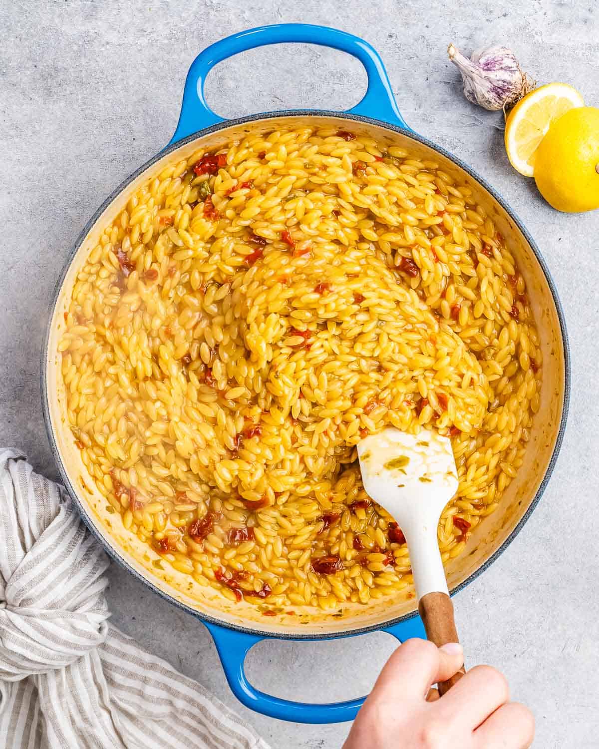 Stirring yellow orzo in a blue skillet with a white spatula.