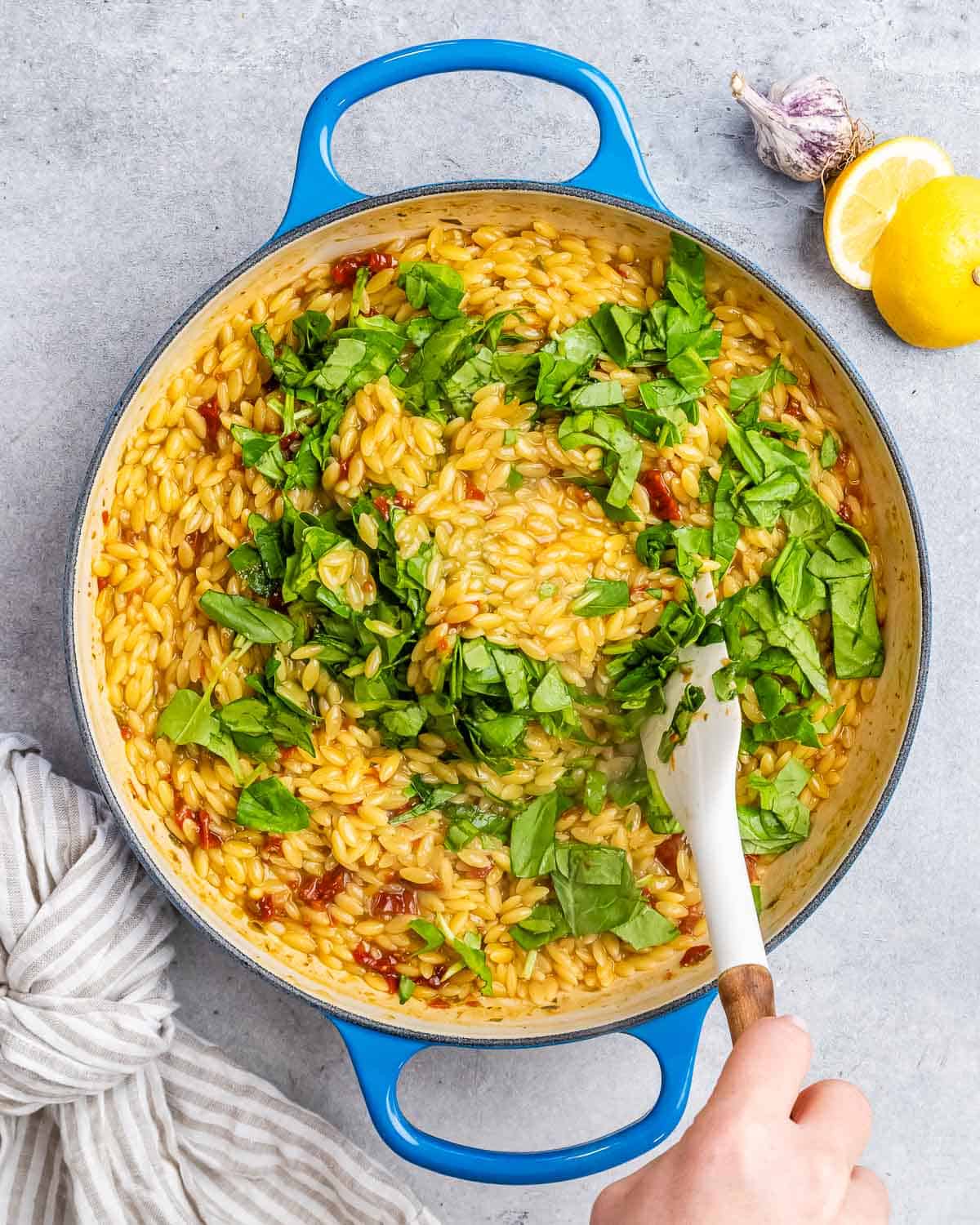 Stirring spinach into a pot of pasta with a white spatula.