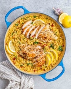 A blue pot filled with yellow orzo and topped with sliced chicken and lemon wedges.