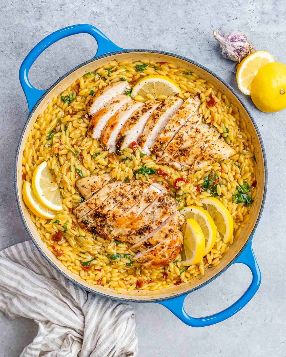 A blue pot filled with yellow orzo and topped with sliced chicken and lemon wedges.