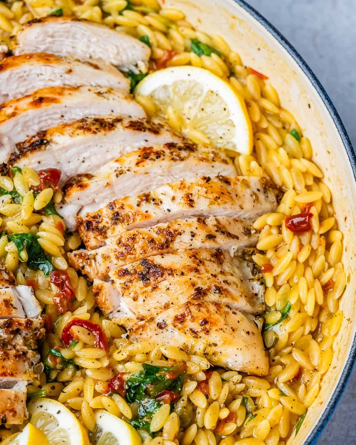 A blue pot filled with yellow orzo and topped with sliced chicken and lemon wedges.