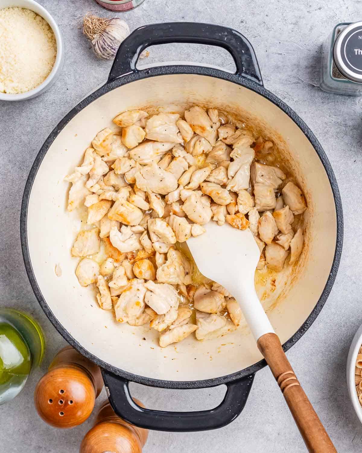 Stirring diced chicken in a pot with a white spatula.