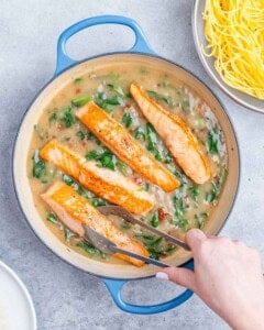 Adding salmon to a pot with a creamy spinach mixture.