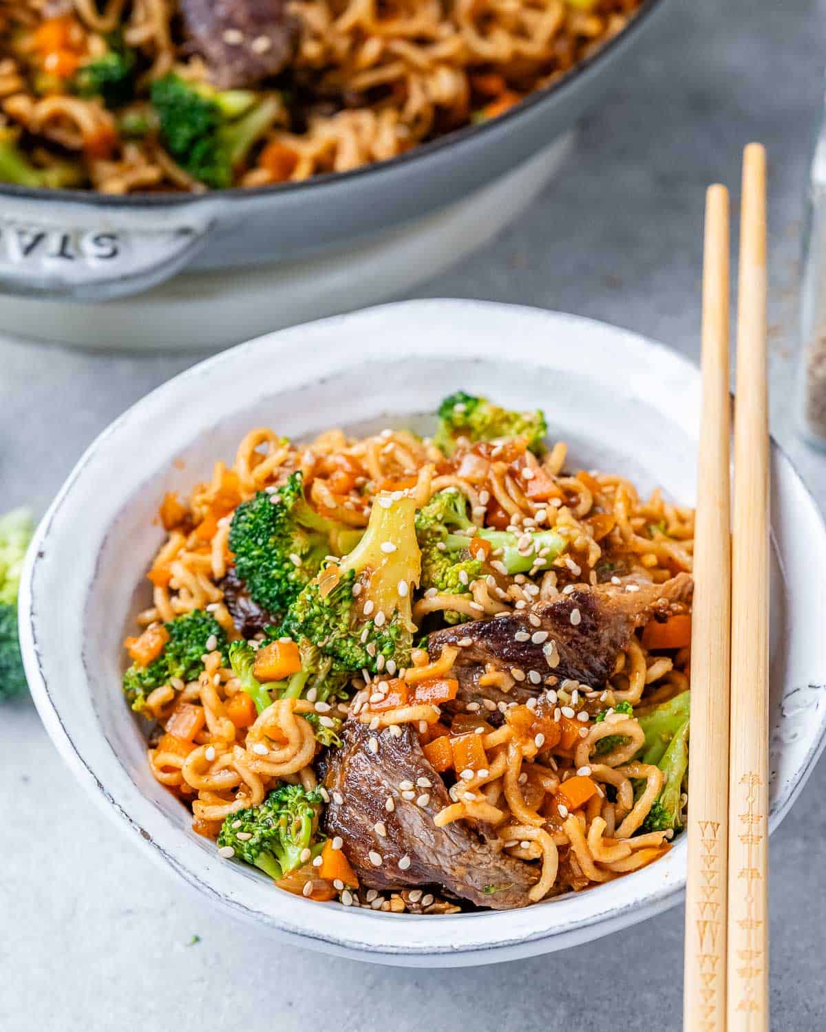 Beef and noodles in a white bowl with chop sticks resting on top.