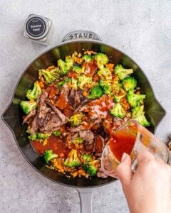 Pouring sauce over a skillet with vegetables and beef.